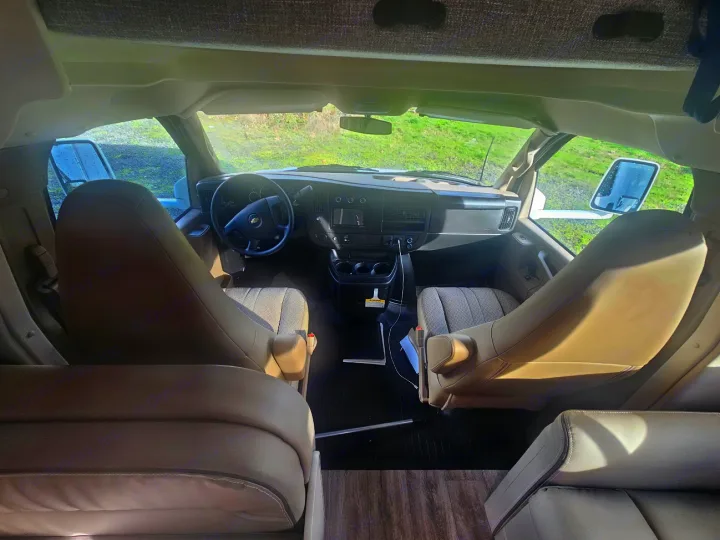 View from the rear of an RV rental's spacious front cabin, showing the driver's area, dash, and passenger seat.. Thor Coleman 28AMC 2024