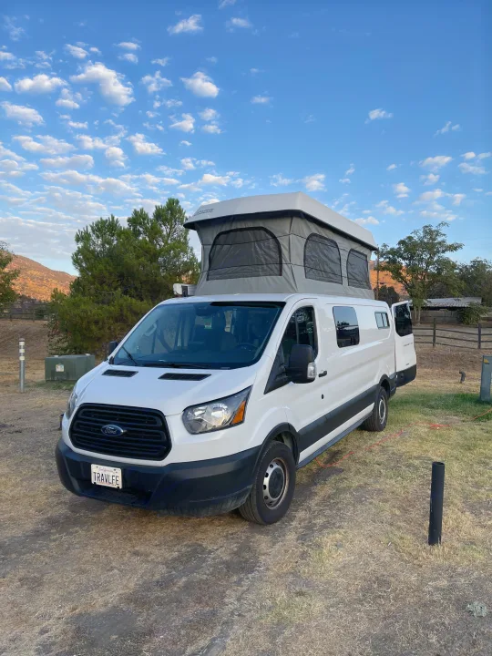 White Ford Transit pop-top camper van, ideal for RV rental adventures, parked in a scenic outdoor setting.. Ford Transit Custom 2019