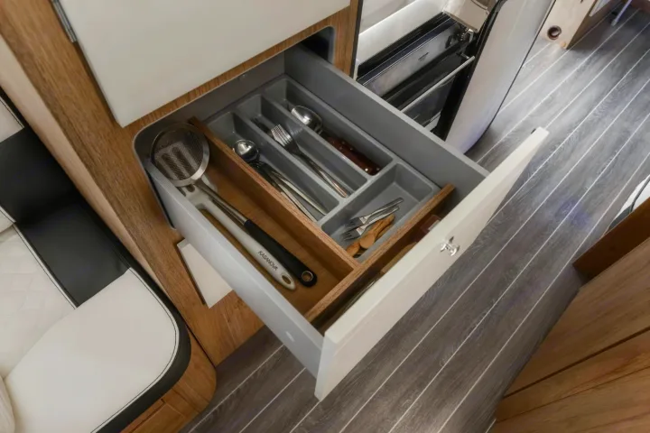 An open, organized kitchen utensil drawer in a modern RV rental, showing a strainer, forks, spoons, and cooking tools.. Roller Team Auto-Roller 746 2025
