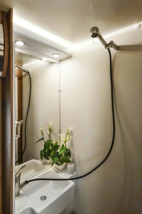 RV rental bathroom: sleek white sink, mirrored vanity with plant reflection, plus a space-saving shower head/faucet combo. Brightly lit.. Roller Team Auto-Roller 746 2025