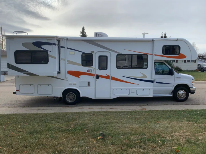 White Class C RV rental, featuring a large extended slide-out and colorful side graphics, parked on a street.. Forest River Sunseeker 2014