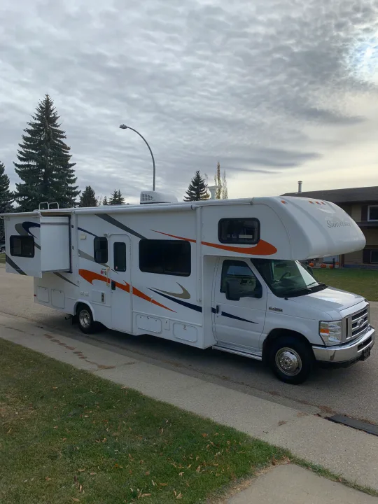 White Sunseeker RV rental parked on a residential street with its slide-out extended under a cloudy sky.. Forest River Sunseeker 2014