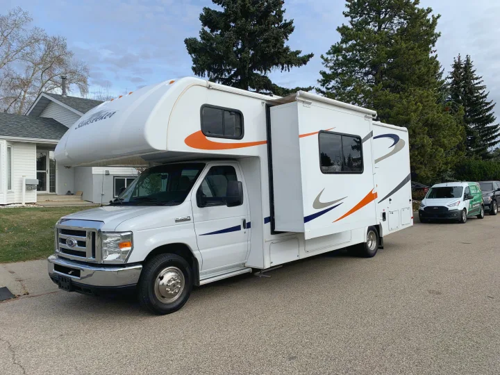 White Sunseeker RV rental, a Class C motorhome with an extended slide-out, parked on a residential street.. Forest River Sunseeker 2014