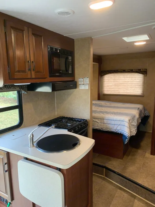 Bright and functional RV rental interior with kitchen (stove, sink, microwave) and adjacent cozy bedroom.. Forest River Sunseeker 2014
