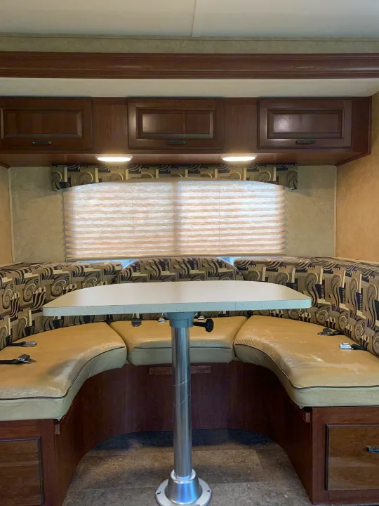Dinette area in an RV rental, featuring U-shaped seating, table, cabinets, and a window.. Forest River Sunseeker 2014