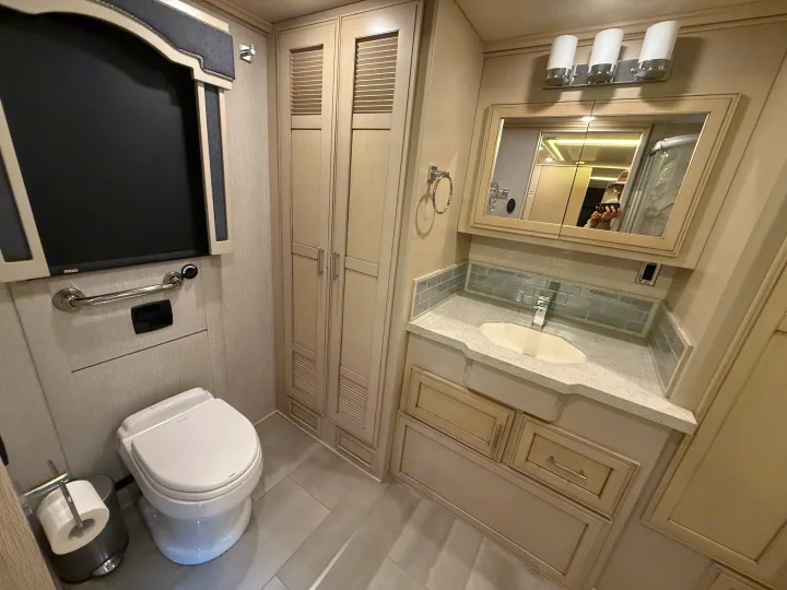Modern RV rental bathroom with toilet, sink vanity, storage, and shower reflected in mirror, offering comfort on the road.. Newmar Ventana 2020