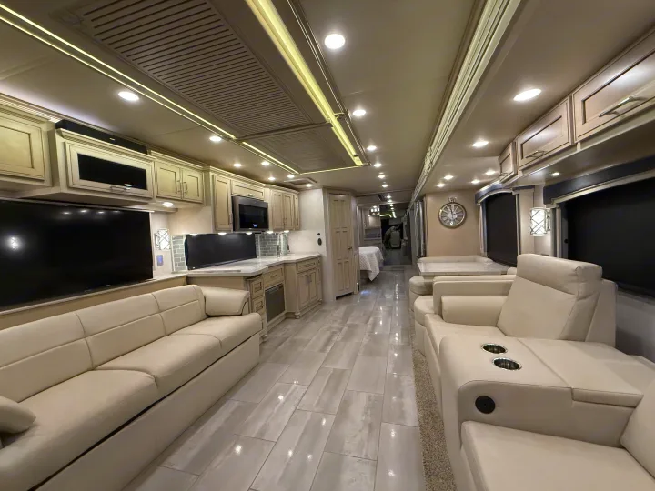 View of a spacious, modern luxury RV rental interior featuring cream sofas, a full kitchen, and light gray tiled floor.. Newmar Ventana 2020