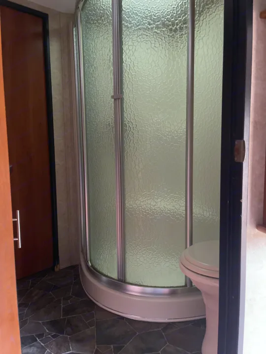 Compact RV rental bathroom with a textured glass shower, toilet, and dark tiled floor. Door visible on left.. Keystone Fuzion 2015