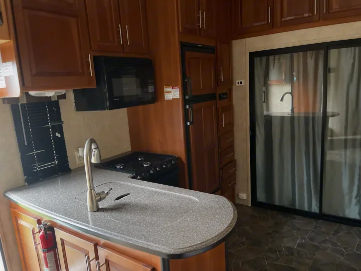 Well-equipped RV rental kitchen with a gray countertop, sink, gas stove, microwave, fridge, and wooden cabinets.. Keystone Fuzion 2015