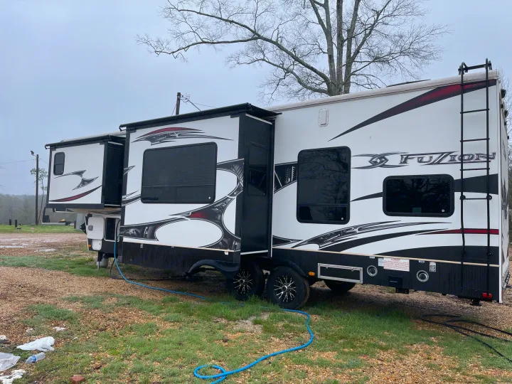 This white and black Fuzion RV, possibly an rv rental, is shown with its slide-outs extended at a campsite under an overcast sky.. Keystone Fuzion 2015