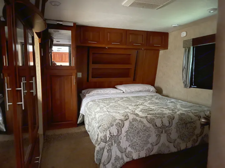 Comfortable RV rental bedroom showing a bed, overhead cabinets, a mirrored wardrobe, and a window.. Keystone Fuzion 2015
