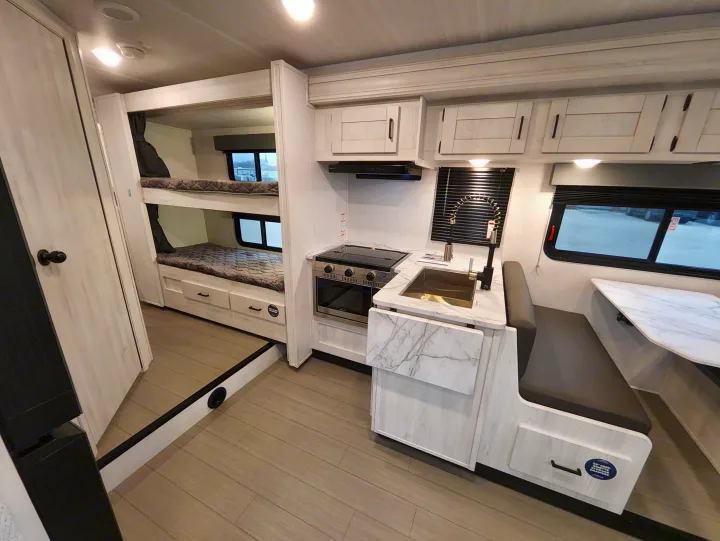 Modern RV rental interior with bunk beds, compact kitchen with stove and sink, and a comfortable dinette. Ideal for travel.. East To West Entrada 2025