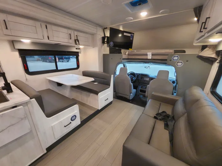 Spacious RV rental interior showing a modern dinette, kitchen, driver's cab, overhead bunk, and a comfy sofa.. East To West Entrada 2025