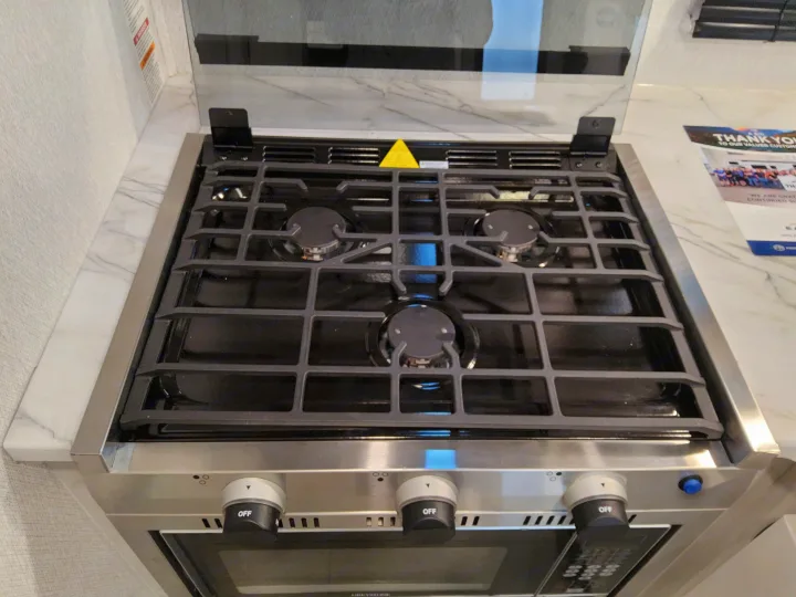 This RV rental kitchen features a sleek gas range with three stovetop burners, an oven below, and accessible control knobs.. East To West Entrada 2025