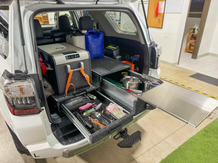 White SUV's custom camping kitchen setup: portable fridge, utensil drawers, pull-out counter. Ideal for an RV rental adventure!. Toyota 4Runner 2024
