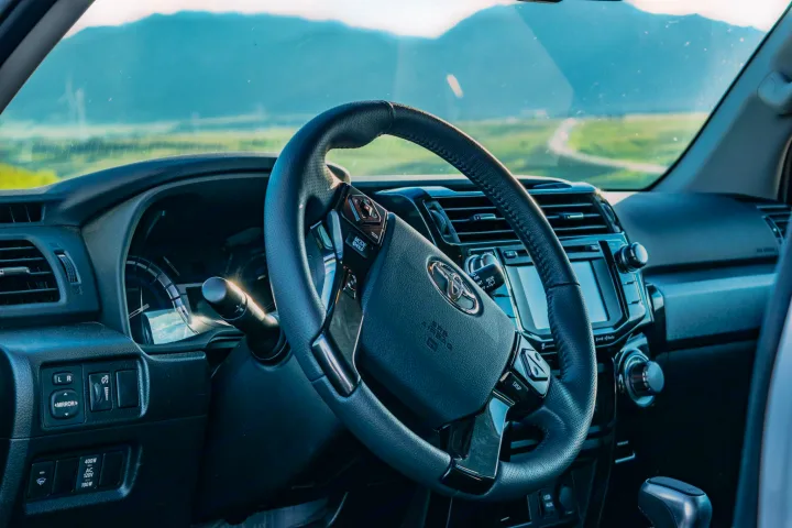 Driver's view from a modern SUV's interior, showing the steering wheel and dashboard with a scenic road ahead. Perfect for an RV rental trip.. Toyota 4Runner 2024