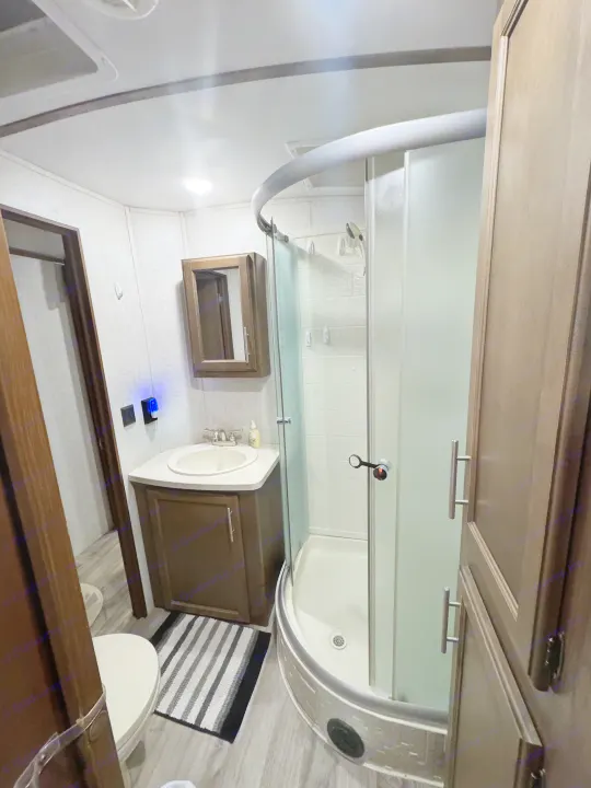 An RV rental bathroom featuring a curved glass shower, sink, mirrored cabinet, and toilet. Compact and functional space.. Keystone RV Cougar 2019