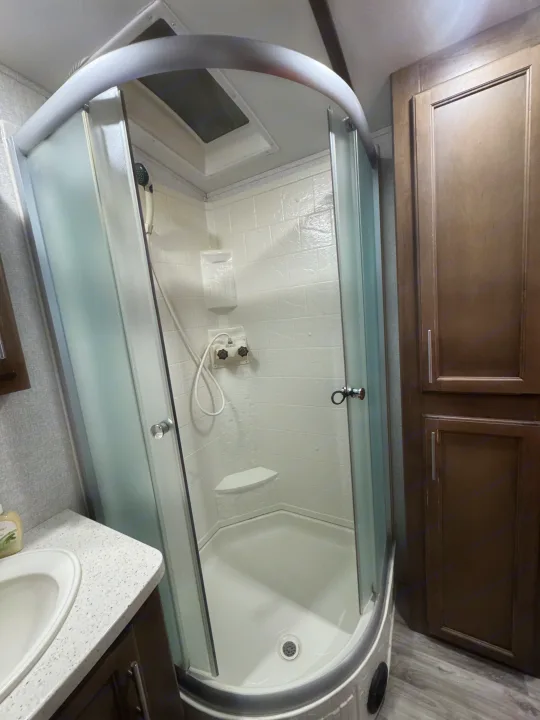 Modern RV rental shower with curved glass, built-in seat, and skylight for a comfortable experience.. Keystone RV Cougar 2019