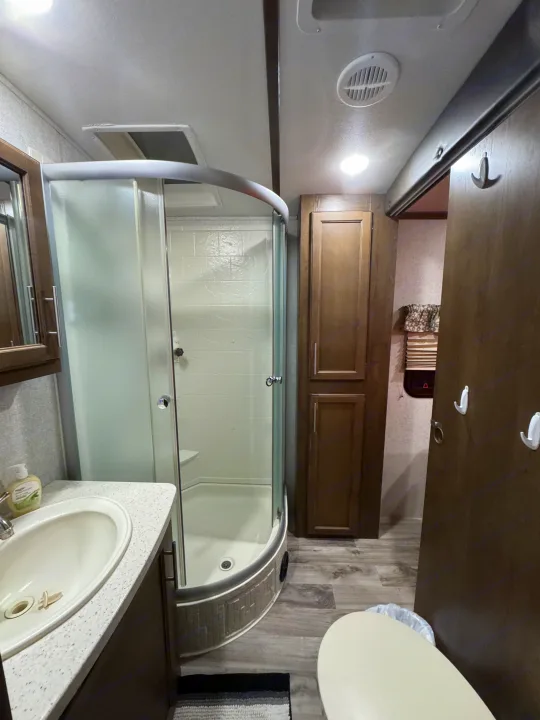 This rv rental bathroom includes a corner shower with a glass door, a sink vanity, toilet, and wood-look cabinetry.. Keystone RV Cougar 2019
