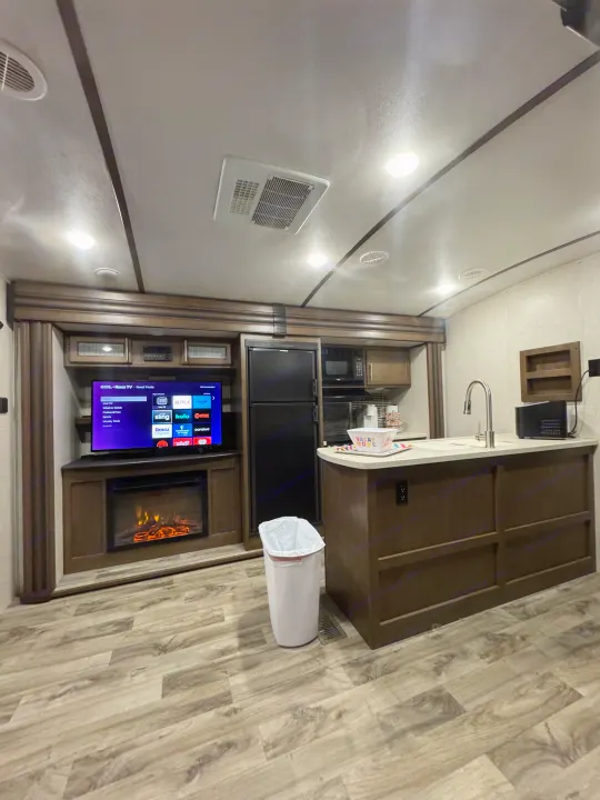 Cozy RV rental interior: kitchen island, Roku TV, electric fireplace, and wood-look flooring in a modern living space.. Keystone RV Cougar 2019
