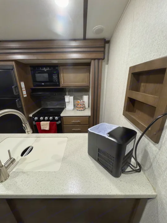 Inside a modern RV rental kitchen, equipped with a sink, stove, microwave, and a countertop ice maker.. Keystone RV Cougar 2019