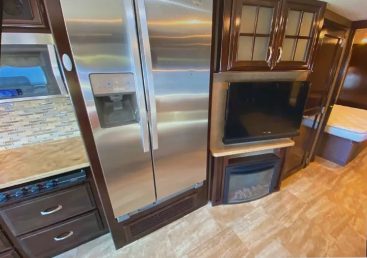 Spacious rv rental interior featuring a modern kitchen with a large refrigerator, cozy fireplace, TV, and comfortable bedroom area.. Thor Challenger 2017