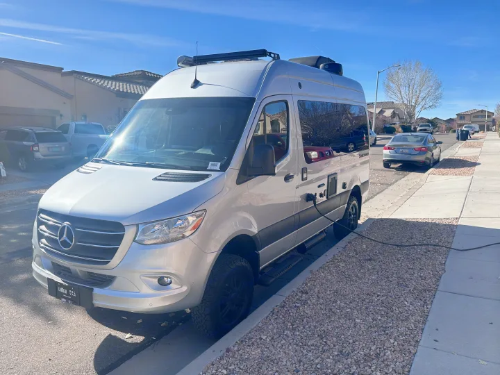 Silver Mercedes Sprinter RV rental, parked on a sunny residential street and plugged in, ready for adventure.. Thor Sanctuary 19P 2025