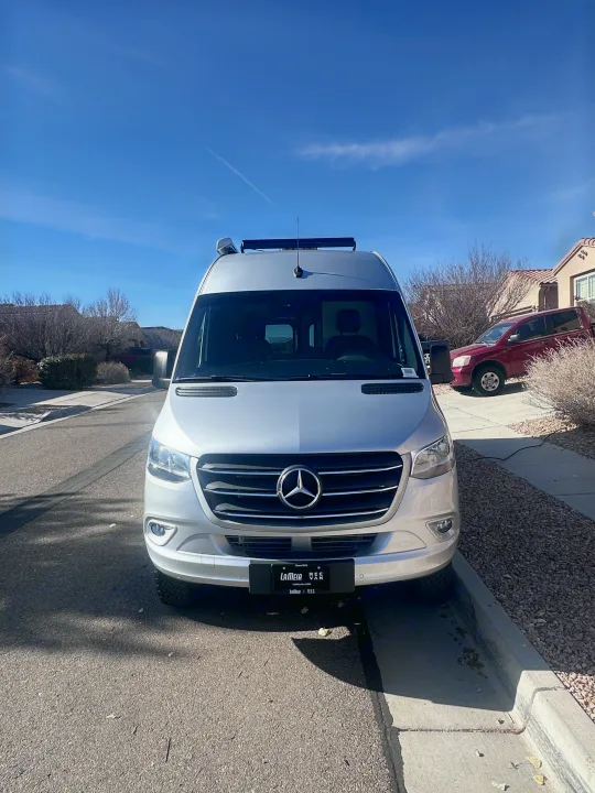 Silver Mercedes-Benz Sprinter van rv rental parked curbside on a sunny day, ready for your next adventure.. Thor Sanctuary 19P 2025