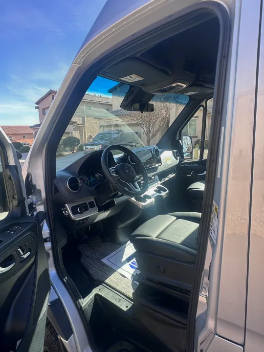RV rental: Driver's side of a Mercedes-Benz Sprinter van with door open, showing cockpit, steering wheel, & digital dash.. Thor Sanctuary 19P 2025