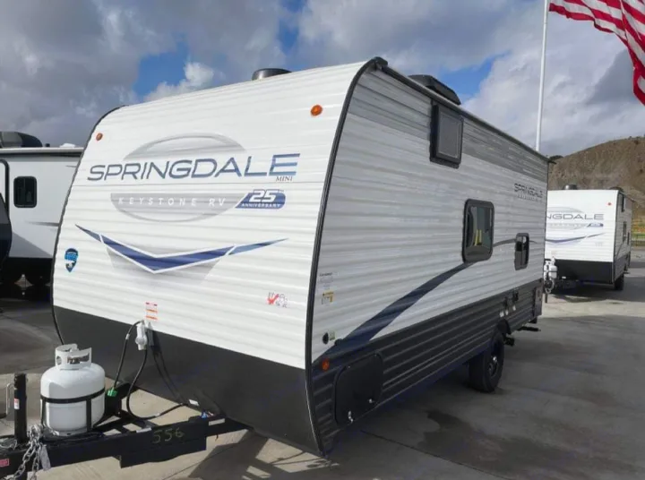 This white Springdale Mini travel trailer with black trim and propane tank is ready as an RV rental.. Keystone RV Springdale 2024