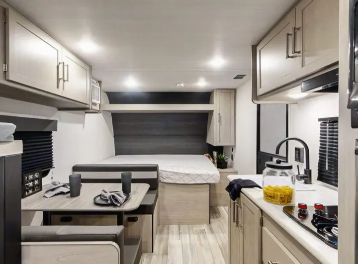 This inviting RV rental interior showcases a functional kitchen, cozy dining booth, and comfortable sleeping area for compact living.. Keystone RV Springdale 2024