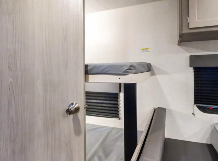 This RV rental interior features modern bunk beds with grey mattresses, a lower sleeping area, and privacy blinds, maximizing compact living.. Keystone RV Springdale 2024