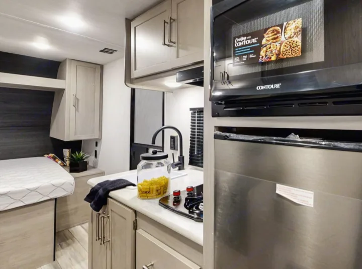 Modern RV rental interior featuring a compact kitchen with microwave, sink, and an inviting bed area.. Keystone RV Springdale 2024