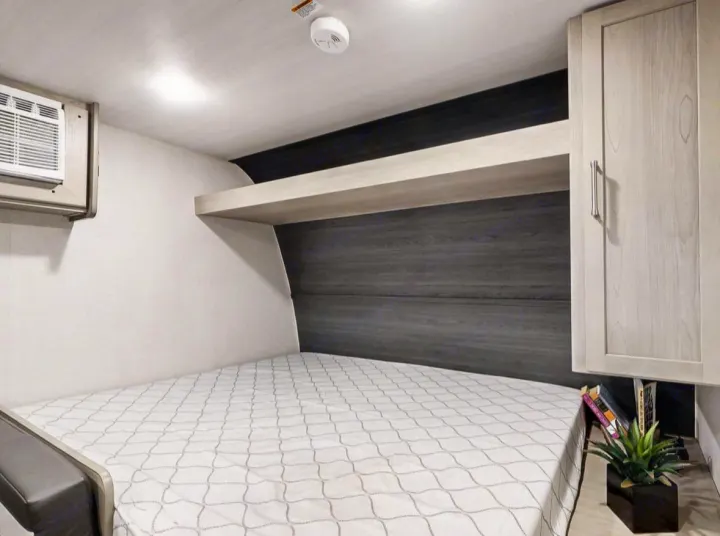 Cozy RV rental bedroom featuring a comfortable bed, AC unit, overhead shelf, and compact storage.. Keystone RV Springdale 2024