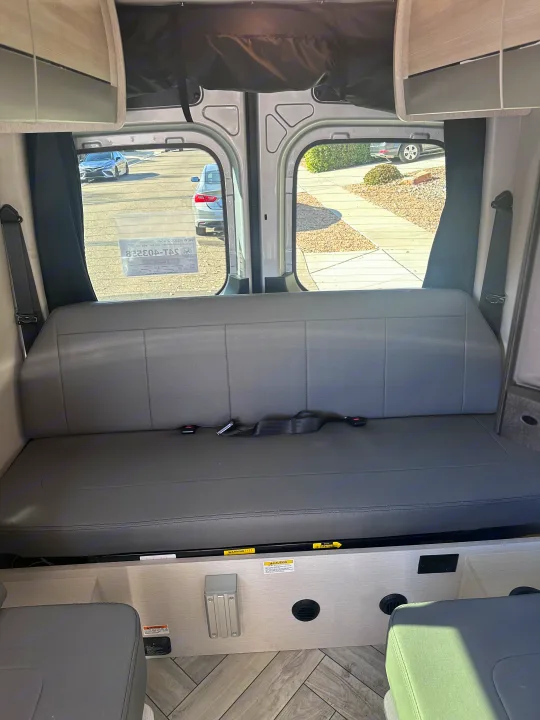 Inside an RV rental: Spacious rear interior featuring a gray bench seat with seatbelts, ample storage, and large windows.. Thor Sanctuary 19P 2025