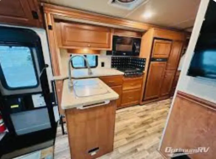Inside this modern RV rental: a well-equipped kitchen with a sink island, microwave, fridge, and wood cabinetry.. Winnebago Vista LX 2017