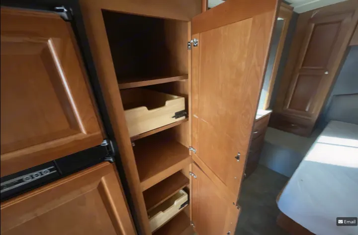 RV rental pantry: Open wooden cabinet with shelves and pull-out drawers, perfect for organizing. Bedroom visible beyond.. Winnebago Vista LX 2017