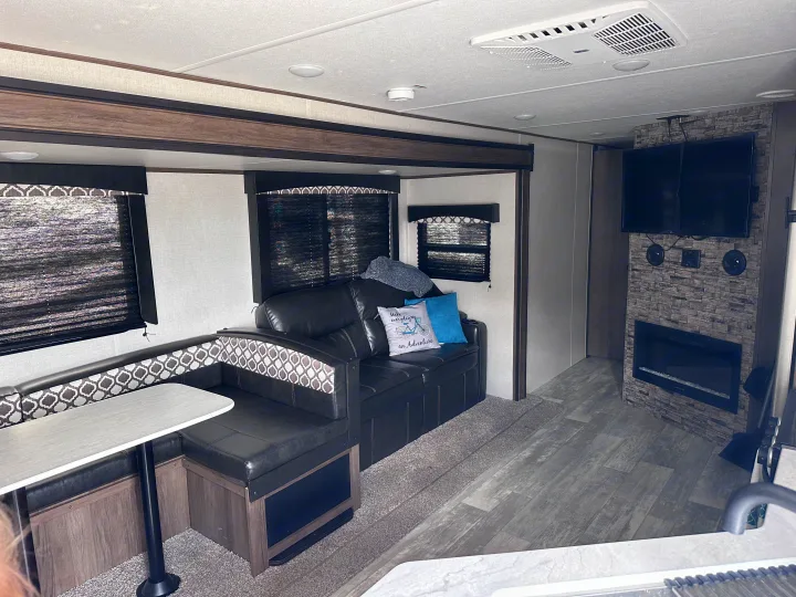 Inside this RV rental: a modern living space with a dinette, plush sofa, and fireplace for comfort on the road.. Forest River Avenger 29QBS 2021