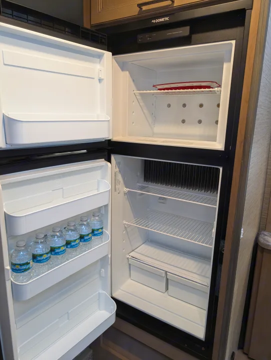 An open Dometic refrigerator in an RV rental, with an empty freezer and bottled water in the fridge.. Thor Four Winds 2021