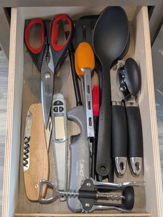 Neatly organized RV rental kitchen drawer with essential tools: shears, spatula, can opener, corkscrew, thermometer, and lighter.. Thor Four Winds 2021