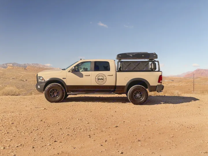 Equipped tan truck with rooftop tent parked in arid mountains; a versatile RV rental for desert adventures.. Dodge Dodge 1 Ton Pu 2018
