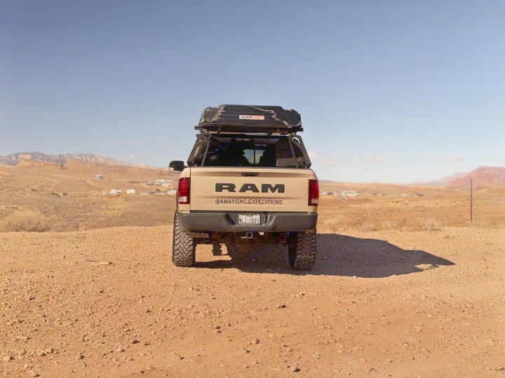 Tan RAM truck with rooftop tent parked on a dirt road in a desert landscape, ideal for an RV rental adventure.. Dodge Dodge 1 Ton Pu 2018