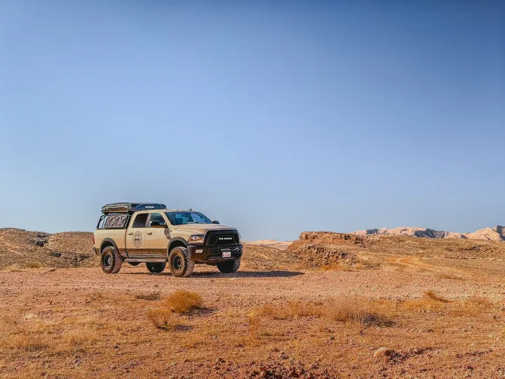 A rugged tan Ram truck with a rooftop tent parked in a dry, rocky desert landscape under a clear sky, perfect for an rv rental adventure.. Dodge Dodge 1 Ton Pu 2018