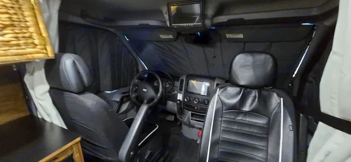 RV rental's front cab: insulated window covers provide privacy, alongside driver/passenger seats, dashboard, and overhead monitor.. Dodge Sprinter 2007