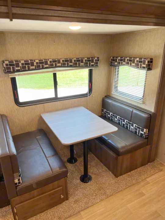 Dark brown benches, a light table, and windows define this RV rental dinette, ideal for a camper's meals.. Dutchmen Coleman Lantern 2019