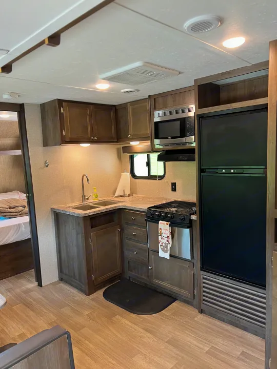 This RV rental features a practical kitchen with a sink, stove, microwave, and refrigerator, plus adjacent bunk beds visible.. Dutchmen Coleman Lantern 2019