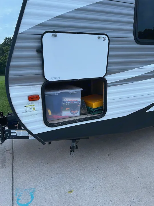 An RV rental's side storage compartment is open, revealing camping gear like Lynx Cap leveling blocks inside, ready for travel.. Dutchmen Coleman Lantern 2019