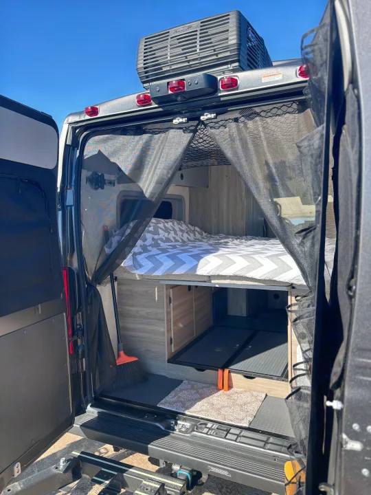 An open RV rental rear reveals a bed, ample storage, and a mesh bug screen for outdoor living comfort.. Winnebago Winnebago 2024