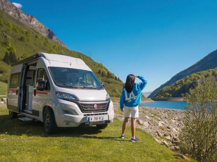 RV rental adventure: White camper van parked on grass by a stunning mountain lake with a dam, person admiring the view.. Pilote V600G EVIDENCE 2025