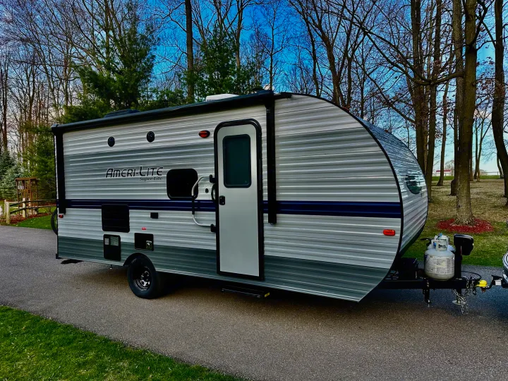 This Ameri-Lite Super-Lite travel trailer, ideal for an rv rental, is parked on a paved lot surrounded by trees, ready for adventure.. Gulf Stream Ameri-Lite Super Lite 2021